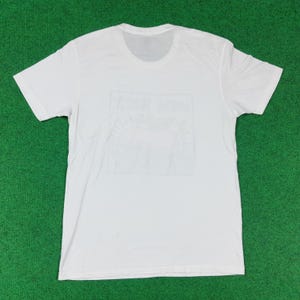 Puede incluir: Camiseta blanca con un gr&aacute;fico descolorido en la parte delantera. El gr&aacute;fico parece ser un sol y texto. La camiseta est&aacute; hecha de un material suave y tiene mangas cortas y cuello redondo.
