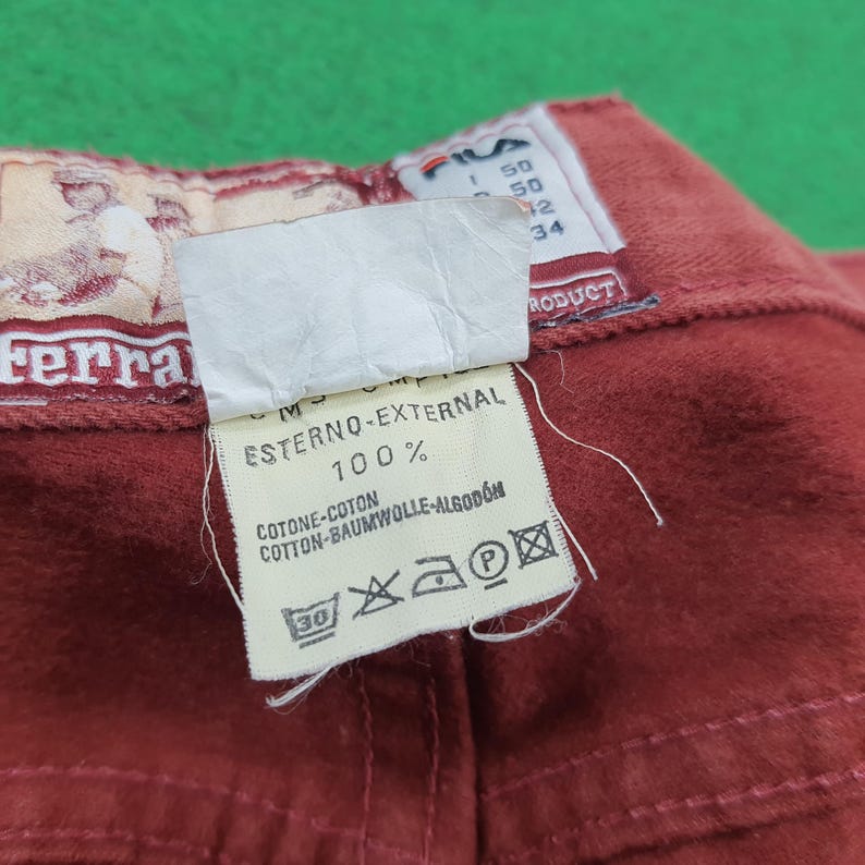 May include: Close-up of a section of red fabric with attached tags. One tag features the brand name "Ferra" and a graphic. Another tag displays text including "ESTERNO-EXTERNAL 100%" and washing instructions.