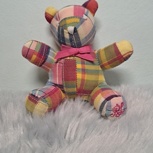 May include: A small stuffed bear made from a patchwork of multicoloured plaid fabric in shades of yellow, pink, blue, and red. The bear features a small pink ribbon tied around its neck and an embroidered RL logo on its right foot.