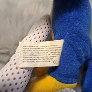 May include: A blue plush toy with yellow feet and a white fabric tag featuring the text: Mary Mayer Corp. Townshend, Vermont. Woody Woodpecker and Friends and related characters are trademarks and copyrights of Walter Lantz Productions, Inc.