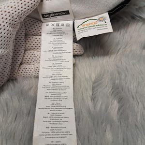Puede incluir: Una etiqueta de cuidado de tela blanca unida a un art&iacute;culo de felpa, con el logotipo de SkyBrands y el texto MADE IN CHINA. Incluye m&uacute;ltiples s&iacute;mbolos de lavado y una etiqueta secundaria con la certificaci&oacute;n Oeko-Tex Standard 100.