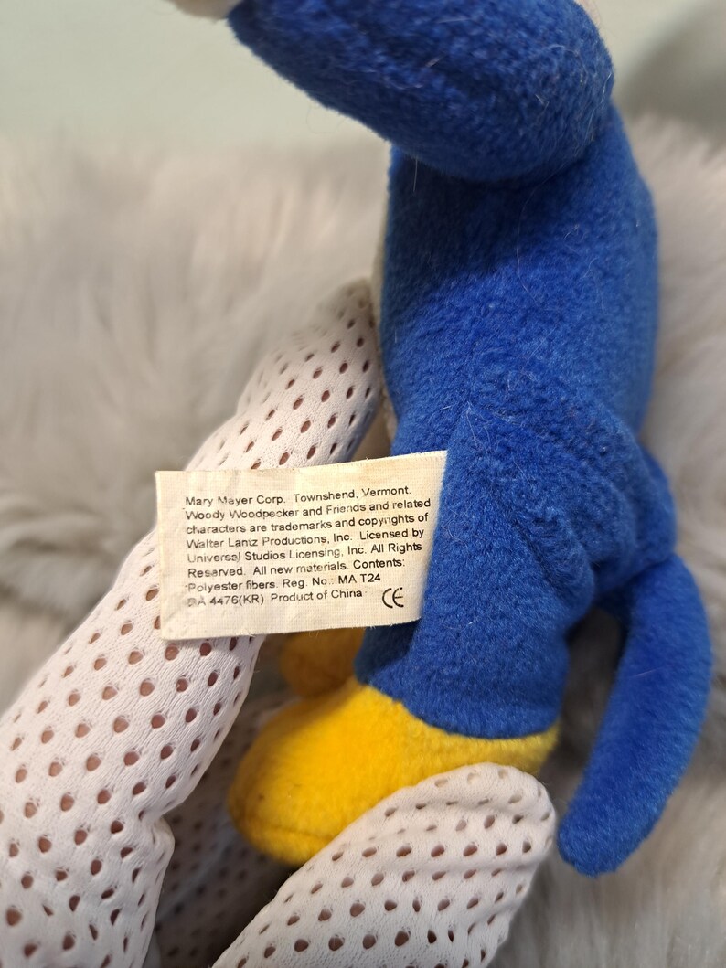May include: A blue plush toy with yellow feet and a white fabric tag featuring the text: Mary Mayer Corp. Townshend, Vermont. Woody Woodpecker and Friends and related characters are trademarks and copyrights of Walter Lantz Productions, Inc.