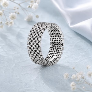 May include: A wide silver-toned band ring featuring five parallel rows of small, clear, round-cut stones set across the entire outer surface. The metal has a textured, darkened finish between the stones, creating a grid-like appearance.
