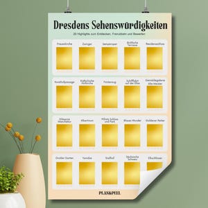 Könnte beinhalten: Ein Poster mit dem Titel "Dresdens Sehenswürdigkeiten" mit 20 Highlights zum Entdecken. Das Poster zeigt goldfarbene Kästchen mit deutschem Text, darunter "Frauenkirche", "Zwinger" und "Semperoper". Die untere rechte Ecke ist leicht eingerollt.