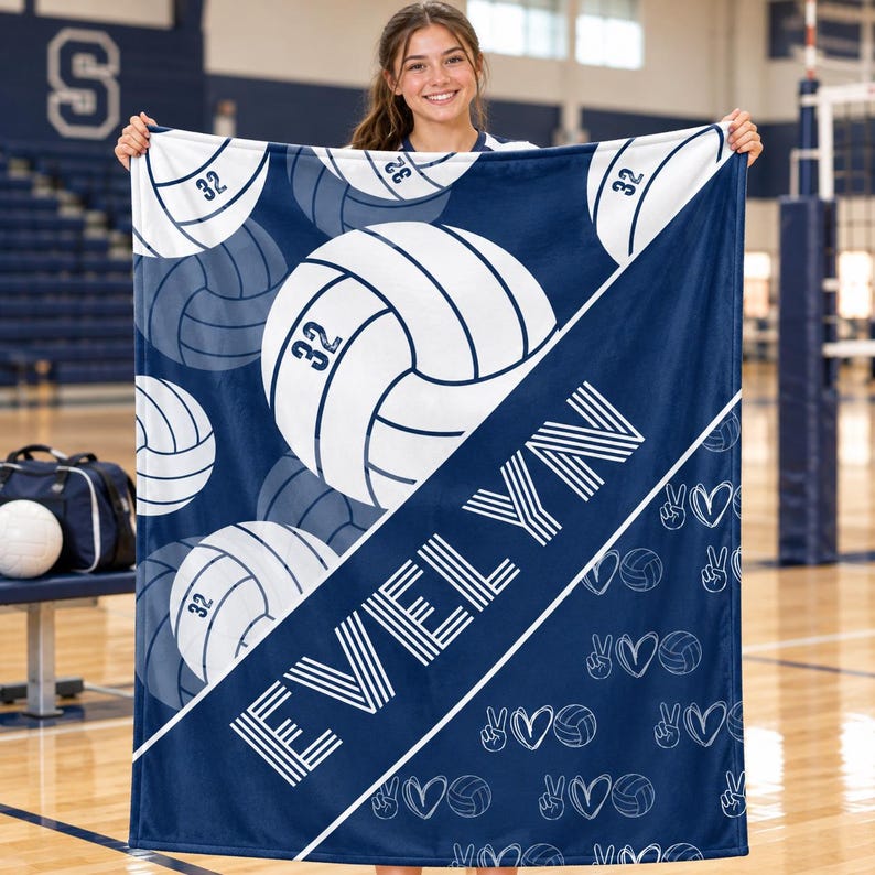 May include: A navy blue and white fleece blanket featuring a repeating pattern of volleyballs with the number 32, the name EVELYN in large white block letters, and small white line-art icons of volleyballs, hearts, and peace signs.