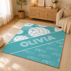 May include: A rectangular area rug in teal featuring a white diagonal stripe with the name OLIVIA in bold letters. The design includes white line art patterns of volleyballs marked with the number 42, heart shapes, and peace hand signs.