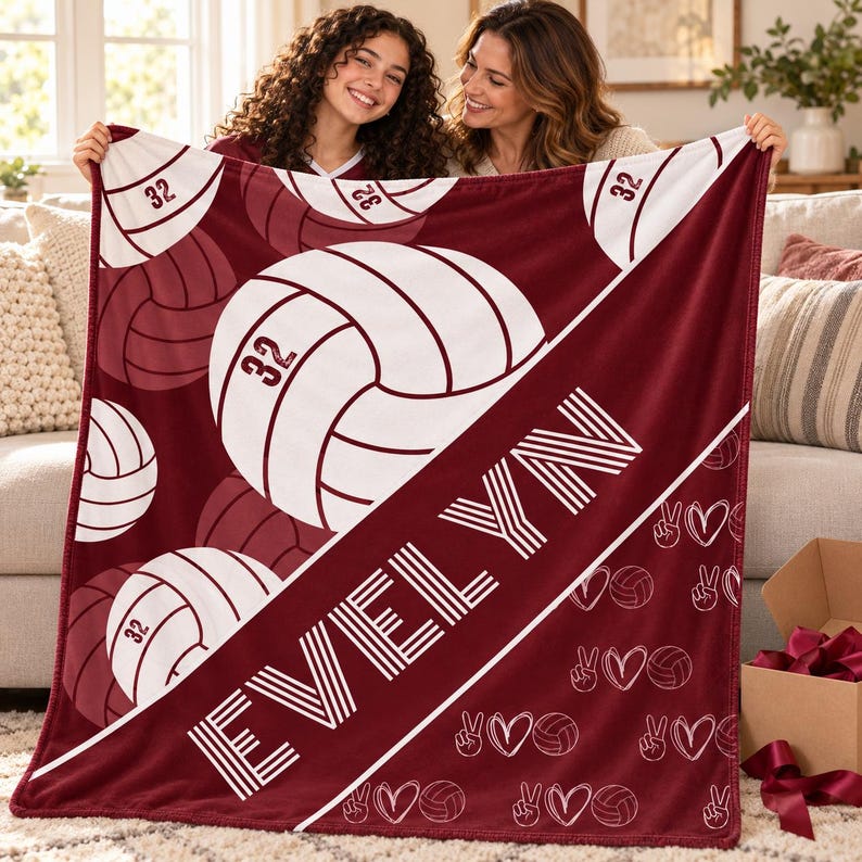 May include: A maroon and white fleece blanket featuring a repeating pattern of volleyballs with the number 32, the name EVELYN in large white block letters, and a smaller pattern of peace signs, hearts, and volleyballs along the bottom edge.