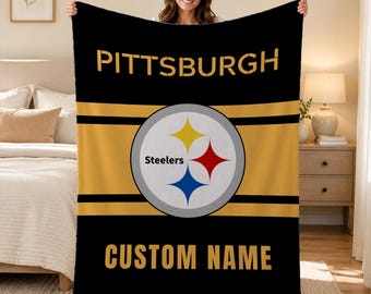 May include: A black and gold fleece blanket featuring the Pittsburgh Steelers logo in the centre. The word PITTSBURGH is printed in gold at the top, and the text CUSTOM NAME is printed in gold at the bottom of the rectangular blanket.