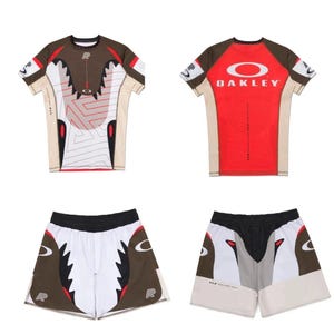 Könnte beinhalten: Ein Sportbekleidungsset bestehend aus einem kurzärmeligen Shirt und Shorts. Das Shirt hat ein braunes, rotes und weißes Design mit dem Oakley-Logo. Die Shorts sind weiß mit braunen und schwarzen Akzenten. Das Set ist für Sport und Freizeitaktivitäten konzipiert.