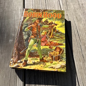 May include: A vintage paperback book with a colorful illustration of Robin Hood and his band of merry men. The cover features Robin Hood aiming an arrow, with a chest of gold coins in the foreground.