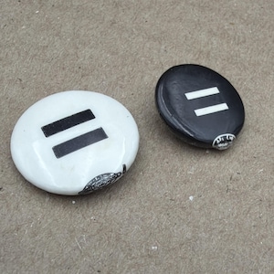 May include: Two oval decorative stones, one white with two black horizontal bars, the other black with two white horizontal bars. Both have a small, detailed design on the edge.
