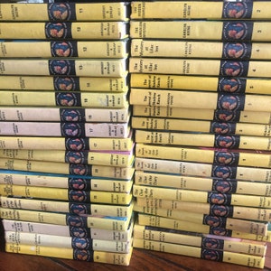 May include: A collection of 20 yellow paperback books with black and red text. The books are stacked in a row and feature the title "The Secret of the Old Clock" and the author "Carolyn Keene".