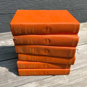 May include: A stack of eight orange hardcover books with gold lettering. The books are all by Zane Grey and feature titles like "The Lost Wagon Train" and "Knights of the Range".
