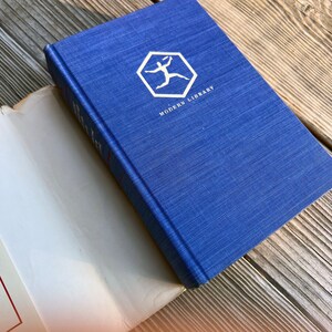 Puede incluir: Un libro de tapa dura azul con el logotipo de Modern Library en la portada. El logotipo es un hex&aacute;gono blanco con una figura de palo blanca corriendo dentro.