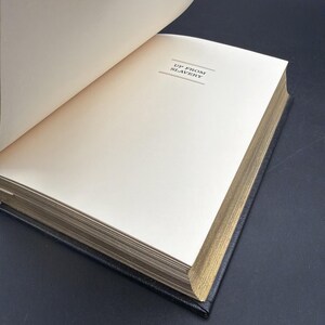 Puede incluir: Un libro abierto con el t&iacute;tulo "UP FROM SLAVERY" impreso en la p&aacute;gina. El libro tiene una cubierta negra y bordes dorados. Las p&aacute;ginas son de color blanquecino y el libro est&aacute; sobre un fondo oscuro.
