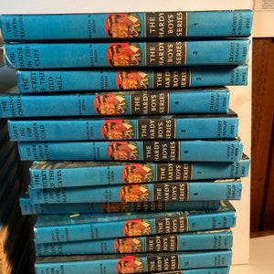 May include: A stack of blue hardback books with the title "The Hardy Boys" and the series number on each book. The books are arranged in order from 1 to 12. The books are all in good condition and have a vintage look.