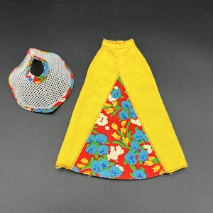 Puede incluir: Una falda amarilla con un estampado floral rojo y una bolsa de malla blanca con un ribete floral. La falda tiene un panel floral triangular. La bolsa es redonda con un agujero en el centro.
