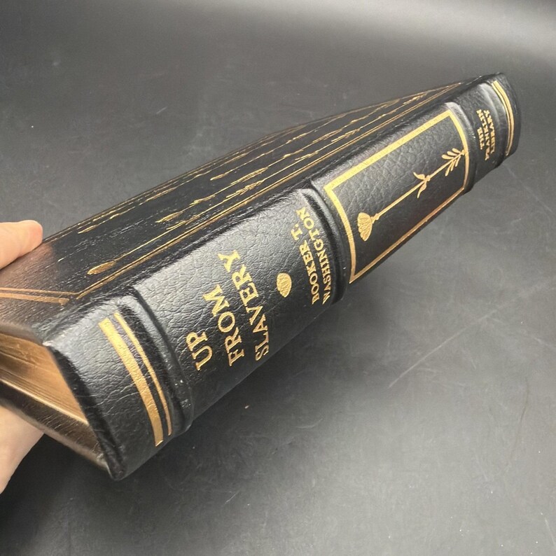 Puede incluir: Un libro de tapa dura negro con letras doradas y detalles decorativos. El libro se titula "Up From Slavery" de Booker T. Washington. El lomo muestra el t&iacute;tulo y el nombre del autor.