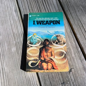 May include: A science fiction novel cover with the title "I, Weapon" by Charles W. Runyon. The cover features a man with long hair and a beard kneeling on a beach with a blue sky and clouds in the background. There are two figures, a woman and a bull, in the background.