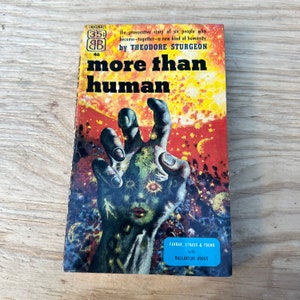 Può includere: Una copertina di un libro tascabile vintage con un'illustrazione colorata di una mano che si estende da un cielo stellato. Il titolo è "Più che umano" di Theodore Sturgeon.