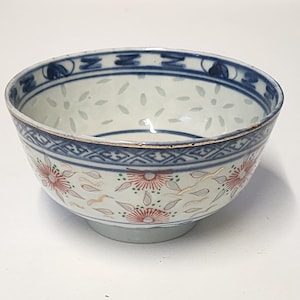May include: A porcelain bowl with a white interior and a blue rim. The bowl features a floral pattern with red and gold accents. The exterior has a blue band with a geometric design.