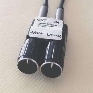 May include: A black audio volume and balance control device with two knobs and a white label. The label reads "OUT", "IN", "Audio Volume and Balance Control", "-Vol+", and "L<->R". The device has two gray cables.