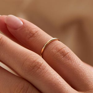 May include: A delicate, thin gold ring is worn on a finger. The ring has a simple, minimalist design, with a smooth, polished surface. The ring is a classic piece of jewelry, suitable for everyday wear.