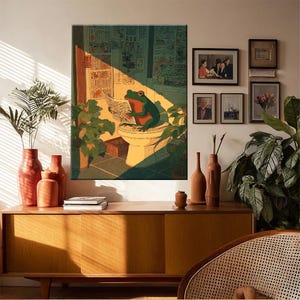 Puede incluir: Una impresi&oacute;n art&iacute;stica enmarcada muestra una rana verde leyendo un peri&oacute;dico en un inodoro. La obra de arte est&aacute; en una habitaci&oacute;n con plantas, un mueble de madera y fotos enmarcadas. La rana tiene detalles rojos y est&aacute; iluminada por la luz solar.