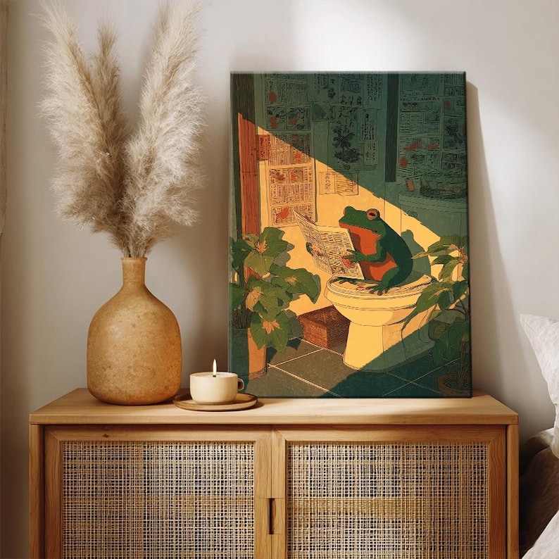 Puede incluir: Una impresi&oacute;n art&iacute;stica enmarcada representa una rana verde leyendo un peri&oacute;dico en un inodoro. La obra de arte est&aacute; ambientada en un ba&ntilde;o con plantas y luz solar. La paleta de colores incluye tonos de verde, naranja y amarillo.