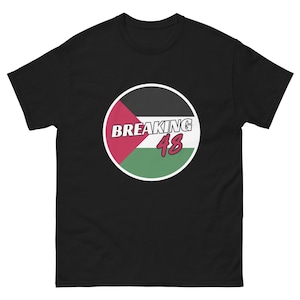 Peut inclure: T-shirt noir avec un motif circulaire portant l'inscription "BREAKING 48". Le motif comprend du rouge, du noir, du blanc et du vert. Le t-shirt est à manches courtes et a un col rond.