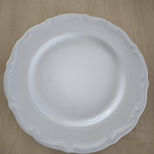 Könnte beinhalten: Ein weißer Keramikteller mit einem gewellten Rand. Der Teller hat ein schlichtes, elegantes Design, ideal zum Servieren von Mahlzeiten. Der Teller ist rund und hat eine glatte, glänzende Oberfläche.