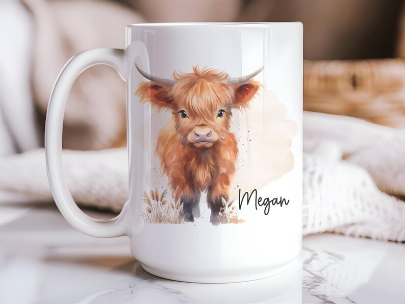 K&ouml;nnte beinhalten: Wei&szlig;e Keramiktasse mit einer Aquarellillustration einer Hochlandkuh. Die Kuh ist in Braun- und Oranget&ouml;nen gehalten, mit dem Namen "Megan" in schwarzer Schrift. Die Tasse hat einen gro&szlig;en Henkel.