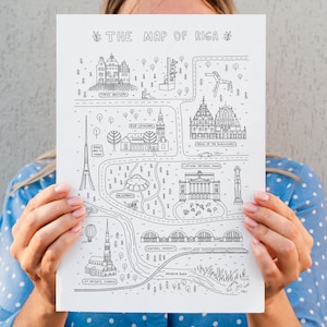 Op de afbeelding: Zwart-wit geïllustreerde kaart van Riga, Letland, met bezienswaardigheden zoals de Sint-Pieterskerk, de Centrale Markt en het Vrijheidsmonument. De tekst "THE MAP OF RIGA" staat bovenaan. De kaart wordt voor een persoon gehouden.