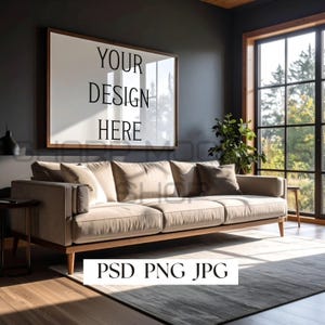 May include: A modern living room featuring a beige sofa with wooden legs and a large framed artwork on the wall. The artwork reads "YOUR DESIGN HERE". A rug and a window with a view of trees are also visible.