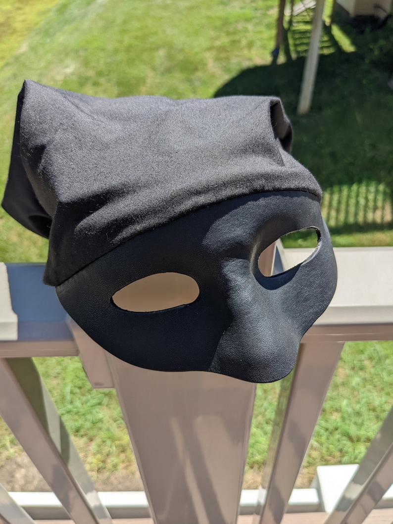 May include: A black masquerade mask with two eye holes. The mask is made of a soft, pliable material and has a simple, elegant design.