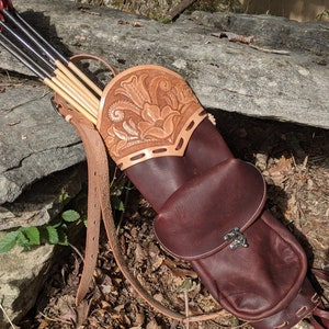 May include: A brown leather quiver with a tooled design and a separate pouch. The quiver is filled with arrows with red fletching.