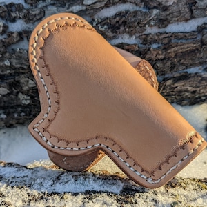 May include: A light brown leather holster with white stitching around the edges. The holster is designed to hold a small firearm.
