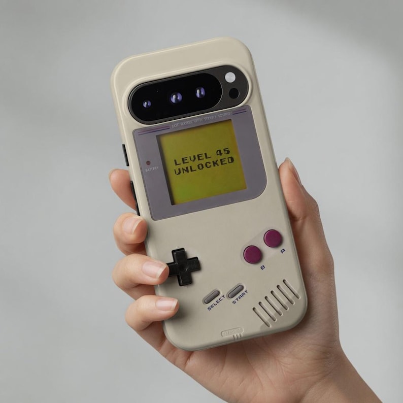 May include: A beige smartphone case designed to resemble a vintage handheld gaming console. The case features a screen displaying the text LEVEL 45 UNLOCKED, a black directional pad, two purple circular buttons, and grey SELECT and START buttons.