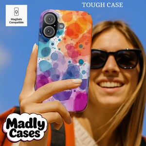 May include: A colorful phone case with a watercolor design featuring orange, red, blue, and purple hues. The case is labeled "Tough Case" and "MagSafe Compatible." The brand name "Madly Cases" is also visible.