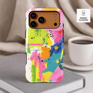 May include: A colorful phone case with an abstract art design. The case features a vibrant mix of pink, yellow, blue, and orange paint strokes and splatters. The case is MagSafe compatible.