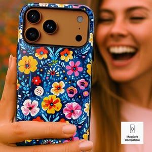 May include: A floral phone case with a dark blue background and a colorful pattern of yellow, pink, and red flowers. The case has a brown camera area and is labeled "MagSafe Compatible".