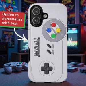 May include: A white phone case featuring a retro video game controller design. The case has a gray directional pad and colored buttons. Text on the case reads "SUPER DAD RAISED ON VIDEO GAMES". The design includes the option to personalize with text.