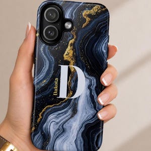 May include: A smartphone case featuring a dark blue and black marbled pattern with gold-colored veins. The case displays a large white letter D and the name Dakota printed in white text on the left side of the letter, with a dual camera cutout.