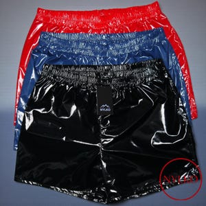 May include: Shiny, high-waisted shorts in red, blue, and black. The shorts have an elastic waistband and a glossy finish. A black tag with the brand name "NYLKO" is attached to the black shorts.