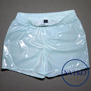 Puede incluir: Pantalones cortos deportivos de color azul claro con cintura elástica. Los pantalones cortos tienen un acabado brillante y lustroso. El logotipo de la marca "NYLKO" es visible en un círculo azul en la parte inferior derecha.