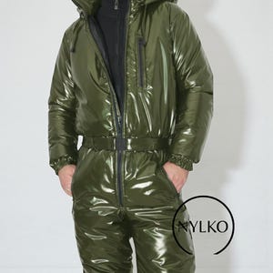 Puede incluir: Mono de nieve de una pieza verde oliva brillante con capucha, cierre de cremallera y cinturón. El mono de nieve tiene un acabado brillante y reflectante. La prenda tiene una cremallera negra y un interior negro. La marca "NYLKO" es visible en la parte inferior derecha.