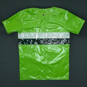 Può includere: Una maglietta verde brillante a maniche corte. La maglietta presenta un design a righe orizzontali bianche e verde scuro sul petto. Il materiale ha un aspetto lucido e riflettente.