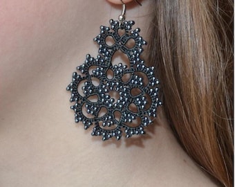 Può includere: Un orecchino nero e ornato con un design floreale, appeso a un orecchio. L'orecchino presenta un motivo traforato dettagliato con piccoli accenti argentati. Il gioiello è realizzato in un materiale scuro, possibilmente metallico.