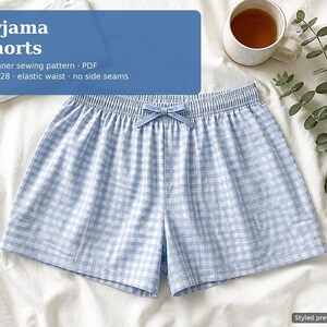 Op de afbeelding: Lichtblauwe en witte pyjamashorts met een vichy-ruitpatroon, een elastische tailleband en een klein strikje in het midden. De tekst op de afbeelding luidt: Pyjama Shorts, Beginner sewing pattern, PDF, UK 6-28, elastic waist, no side seams.