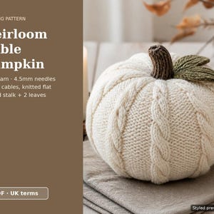 Op de afbeelding: Een crèmekleurige gebreide pompoen met verticale kabelpatronen, een bruine geribbelde steel en twee groene bladeren. De tekst luidt: Knitting Pattern, Heirloom Cable Pumpkin, Aran yarn, 4.5mm needles, 6 rope cables, knitted flat, Ribbed stalk + 2 leaves, PDF, UK terms.